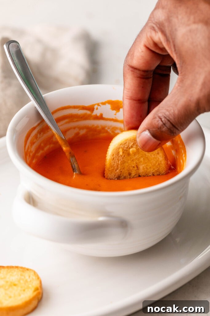 Creamy Sheet-Pan Roasted Tomato Soup 14 dipping a garlic crostini in a bowl of creamy roasted tomato soup