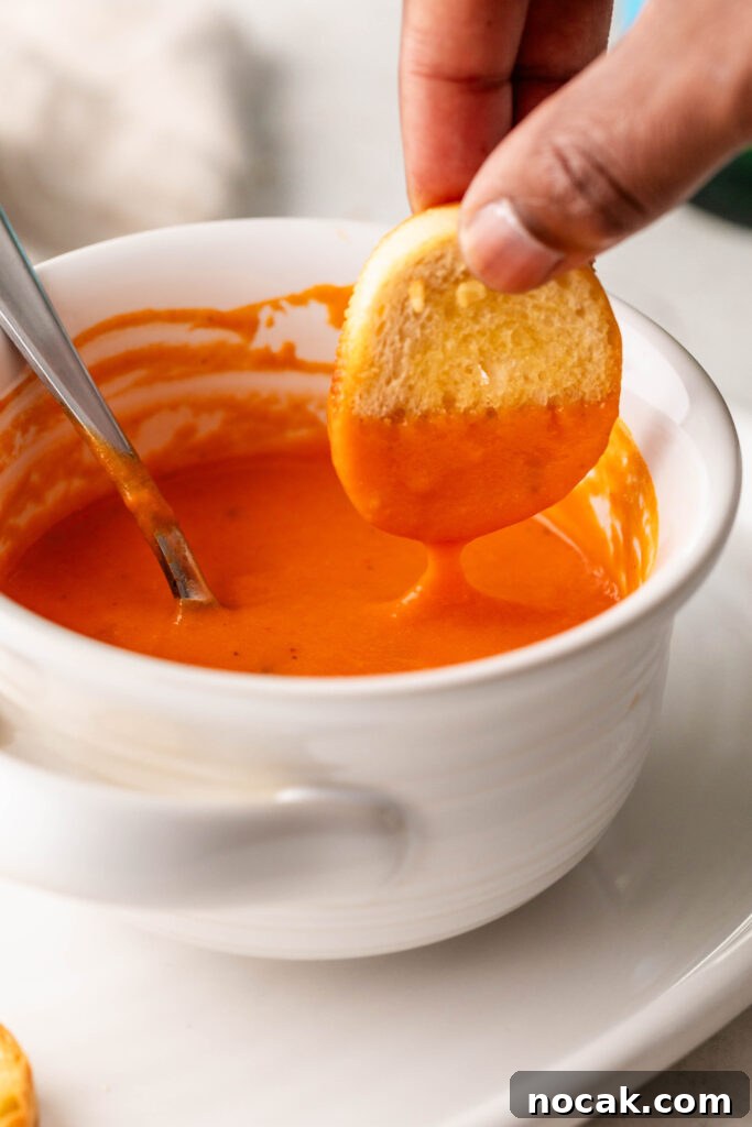 Creamy Sheet-Pan Roasted Tomato Soup 15 dipping a garlic crostini in a bowl of creamy roasted tomato soup