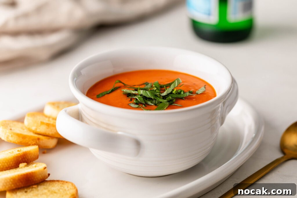 Creamy Sheet-Pan Roasted Tomato Soup 16 bowl of creamy roasted tomato soup topped with fresh basil on a plate with garlic crostini and a gold spoon