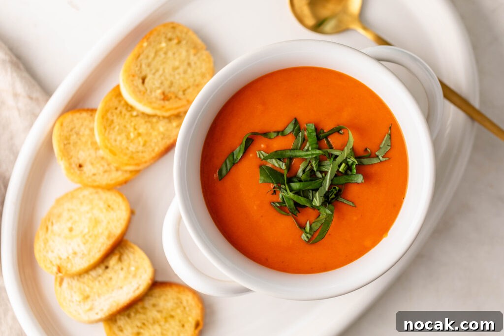 Creamy Sheet-Pan Roasted Tomato Soup 17 bowl of creamy roasted tomato soup topped with fresh basil on a plate with garlic crostini and a gold spoon