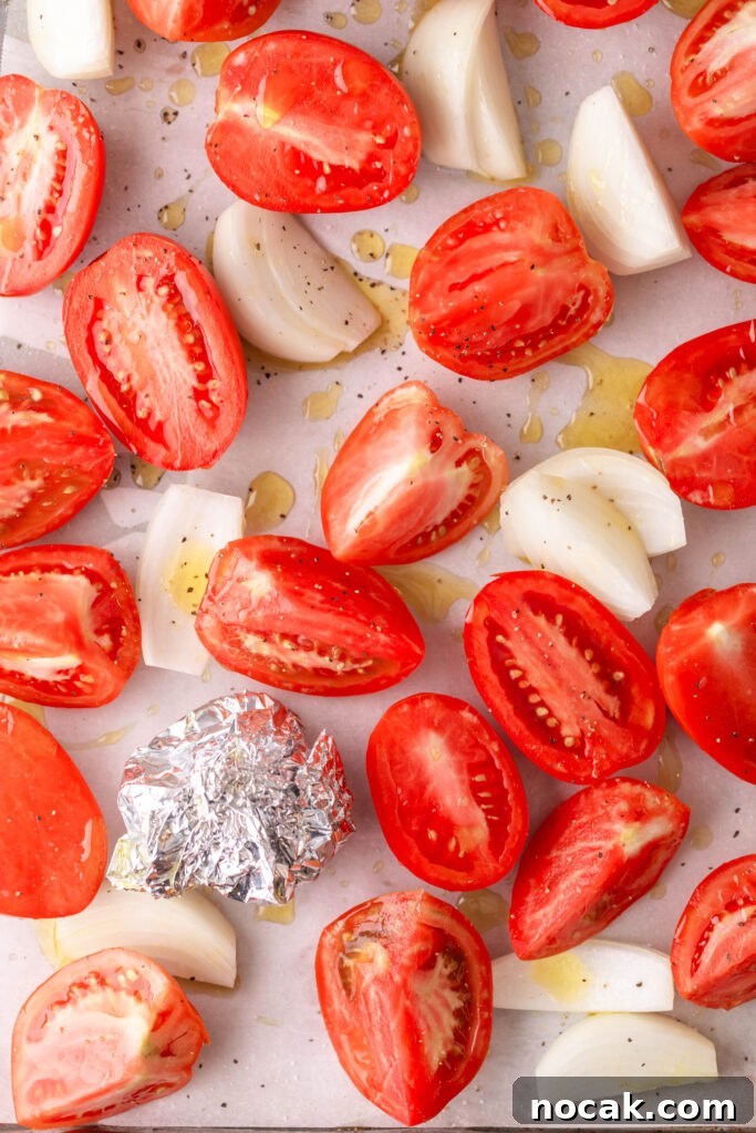Creamy Sheet-Pan Roasted Tomato Soup 8 oiled and seasoned tomatoes and onions with wrapped garlic on a parchment lined sheet pan