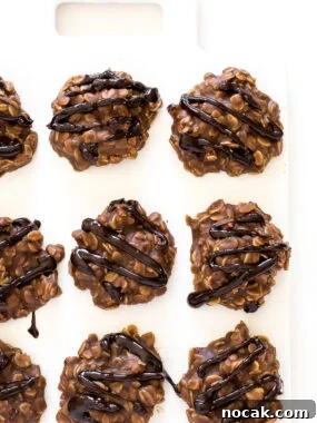 Chocolate oatmeal cookies with chocolate drizzle laid in rows on white cutting board.