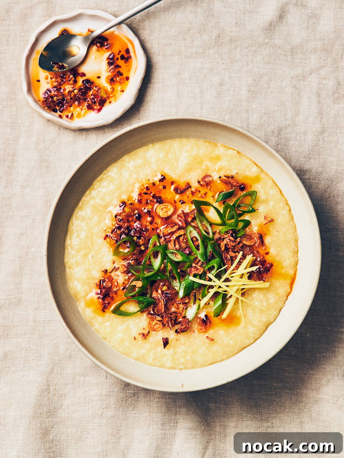 A bowl of vegan congee with homemade chili garlic oil, crispy shallots, scallions, and ginger on top.