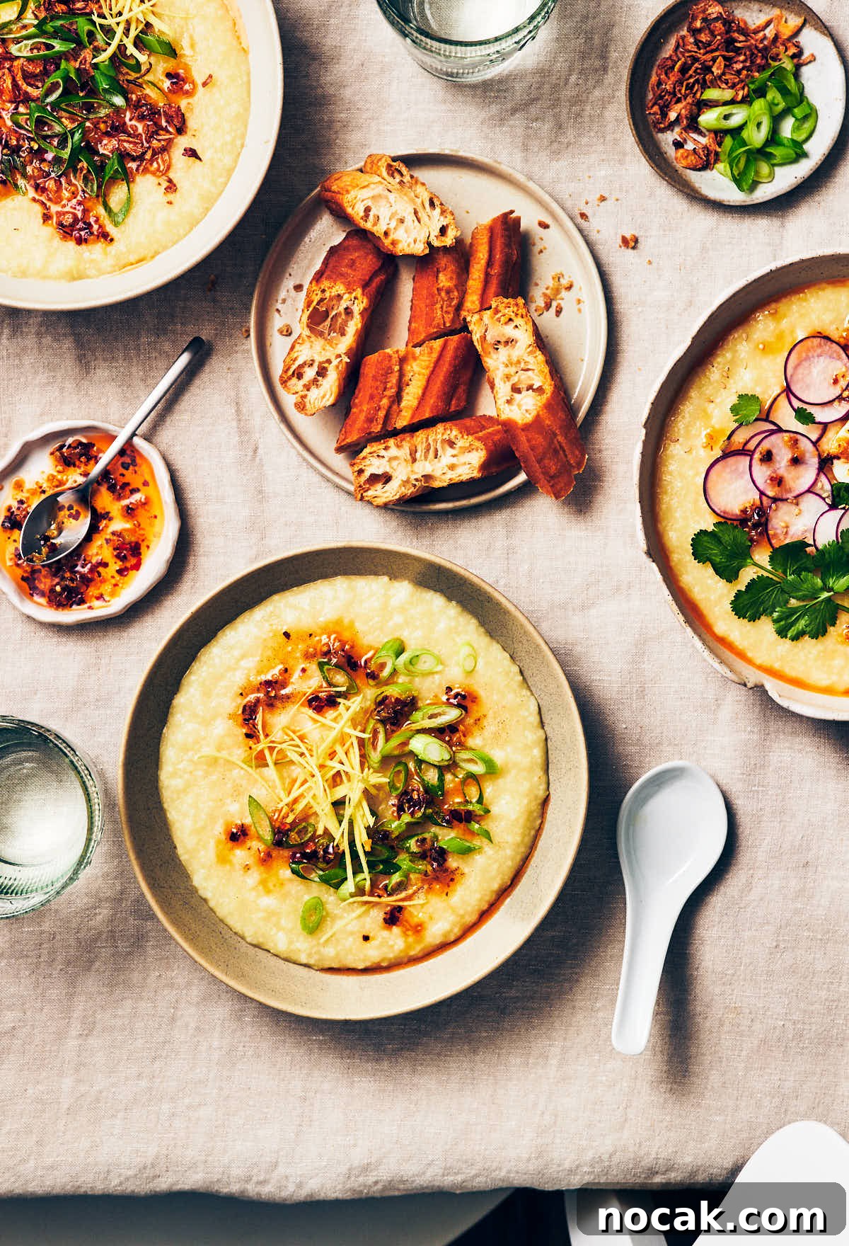 3 bowls of vegan congee with different toppings on a dining table, with a plate of Chinese donuts (youtiao) and glasses of water