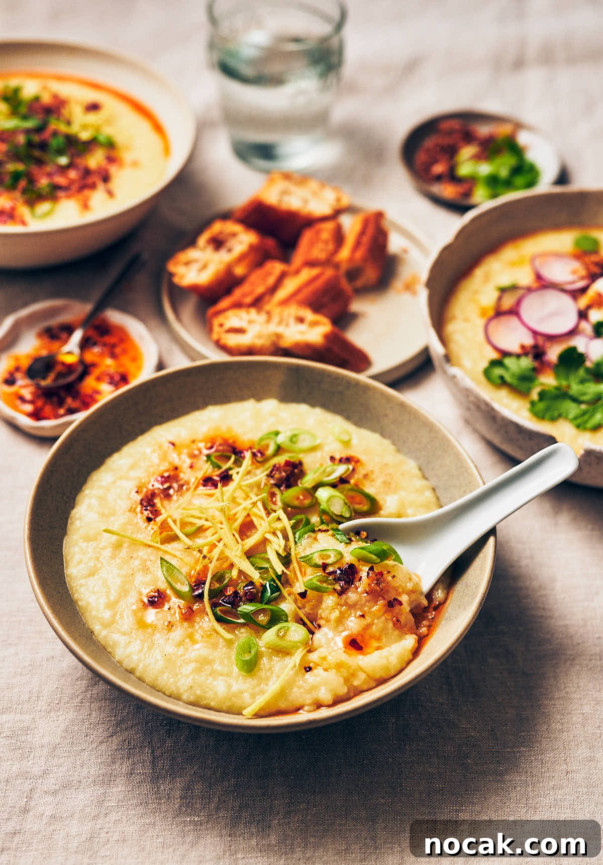 A bowl of vegan congee topped with chili garlic oil and scallions, with a white Chinese spoon scooping out some congee.
