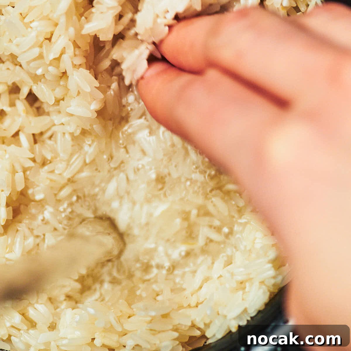 Rice being rinsed in a fine mesh sieve under running water, with a hand swirling the grains of rice.