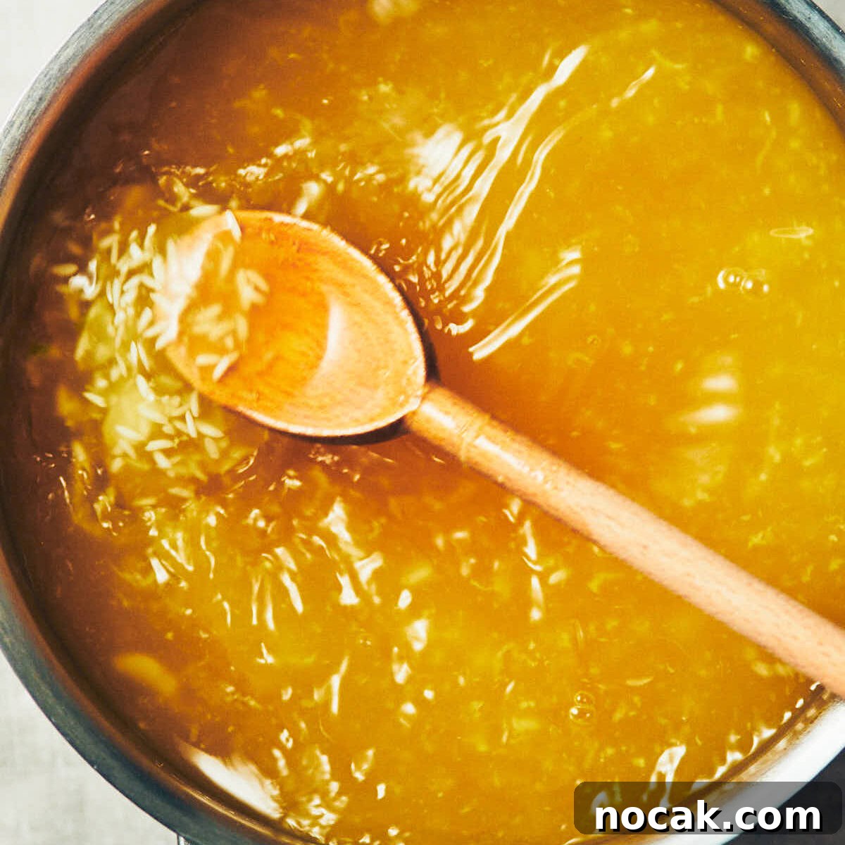 A spoon stirring vegetable stock, ginger, and garlic, into a pot of rice for congee.