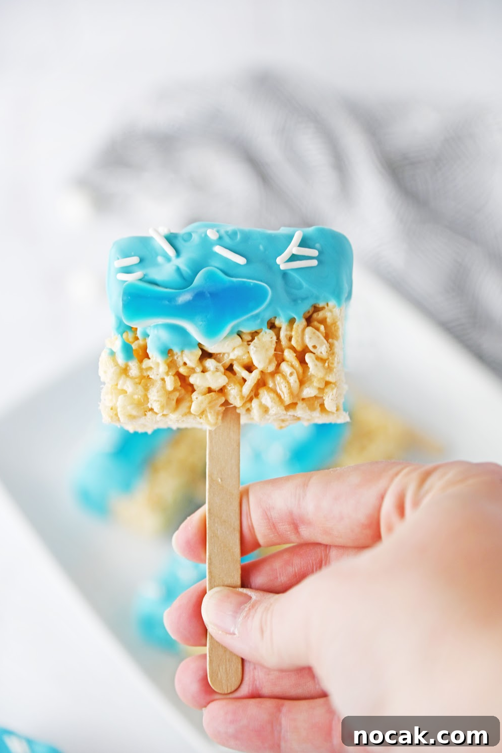 Shark-Themed Rice Krispie Treats: Fun Party Dessert Recipe 3 A hand holding a shark Rice Krispie treat pop made with a gummy shark.
