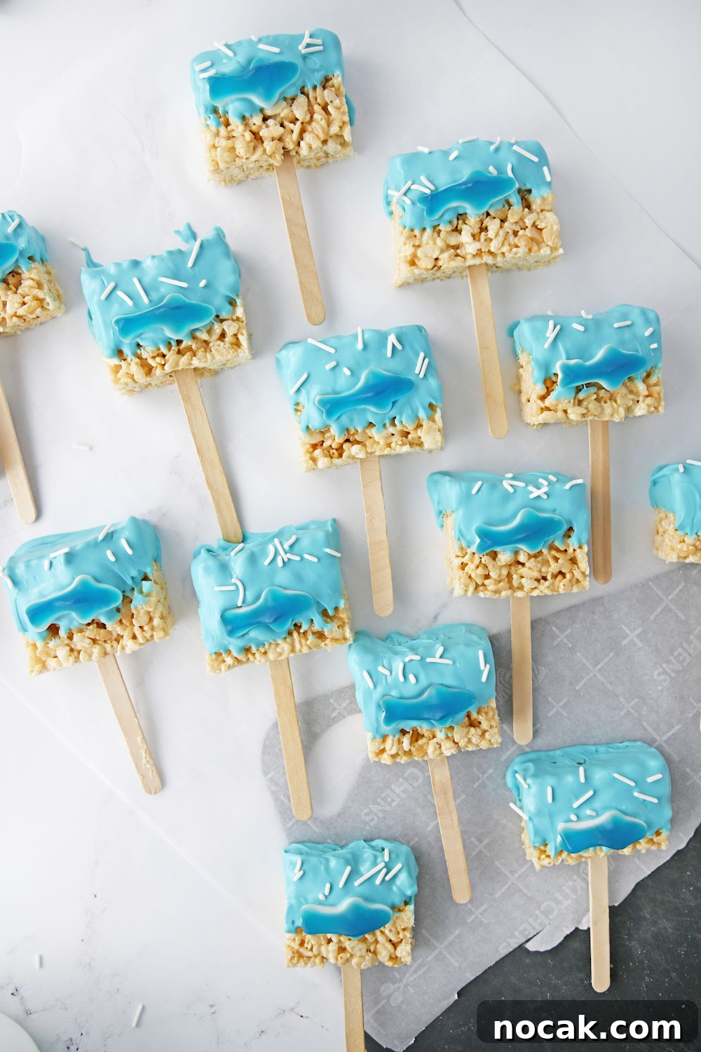 Shark-Themed Rice Krispie Treats: Fun Party Dessert Recipe 4 12 shark Rice Krispie treat pops made with a gummy shark laying on parchment paper.