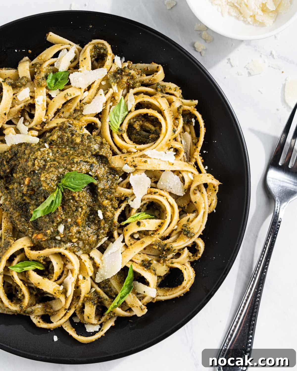 Black Plate with Thai Basil Pesto Pasta topped with a dollop of Thai Basil Pesto, shaved Parmesan cheese, and Thai Basil leaves.