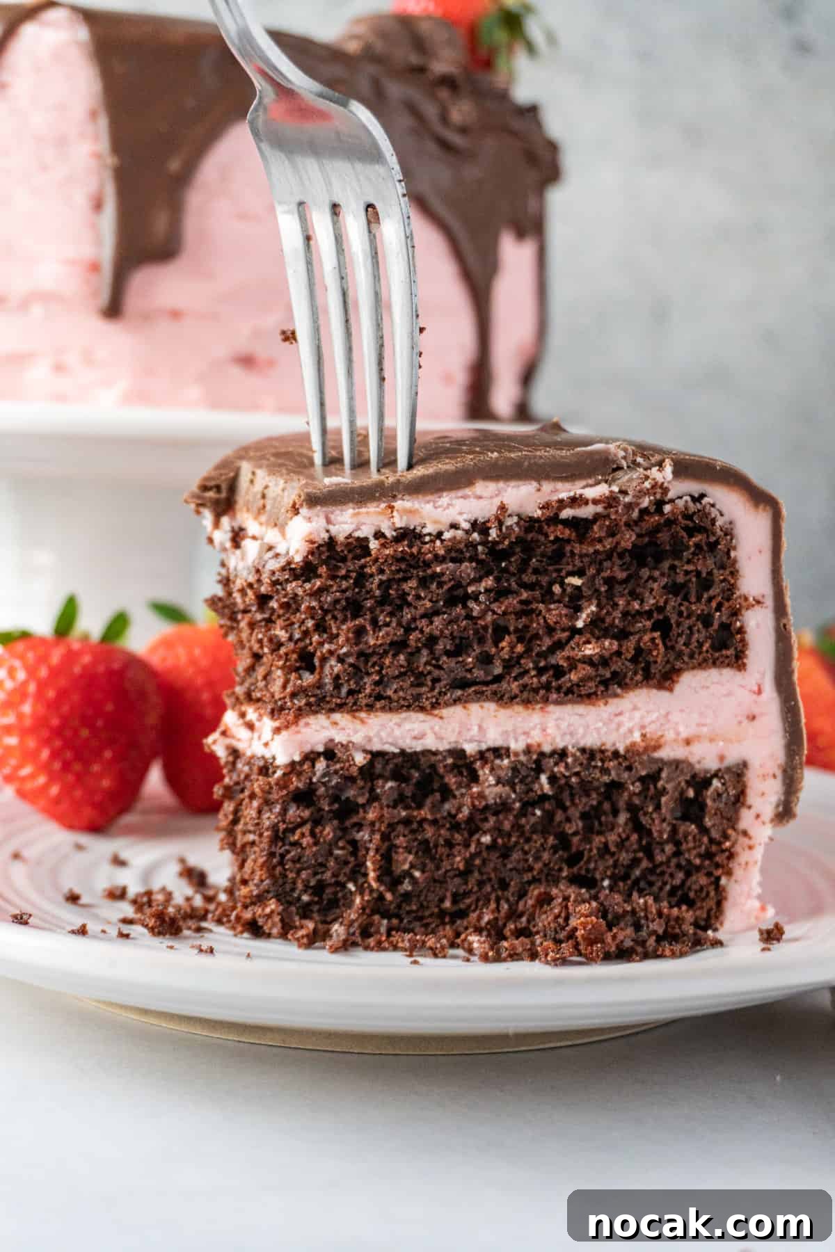 Chocolate Strawberry Layer Cake with Luscious Ganache 2 sticking a fork into a slice chocolate cake with pink frosting.