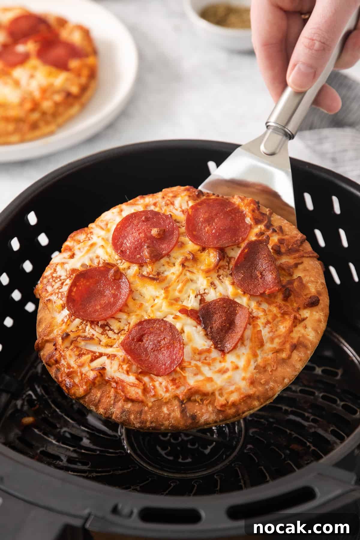 Removing pizza from air fryer Pizza on a spatula being lifted out of the air fryer.