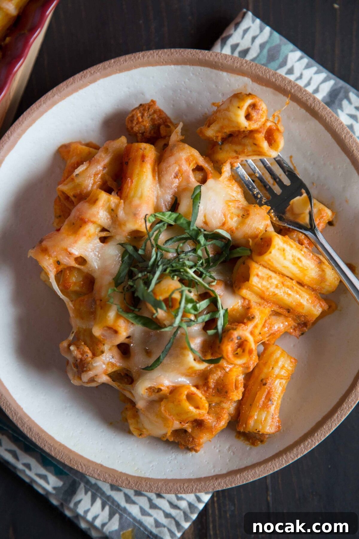 25 Baked Ziti Recipes for Crowd Pleasing Italian Dinners 2 baked ziti in a cream and brown bowl, topped with basil.