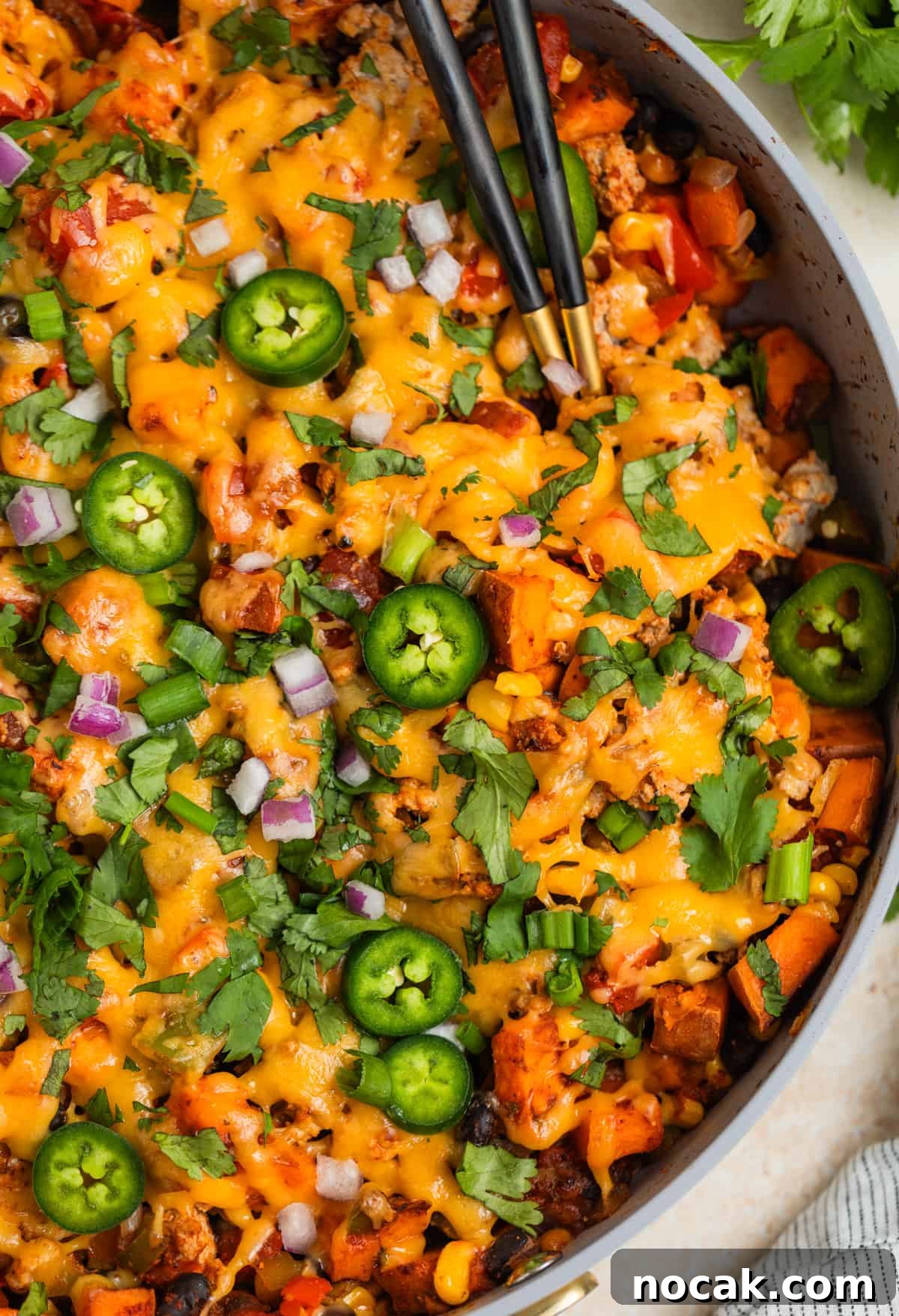 One-Pan Ground Turkey and Sweet Potato Skillet 11 Skillet with ground turkey and sweet potatoes topped with melted cheese and serving utensils scooping in.