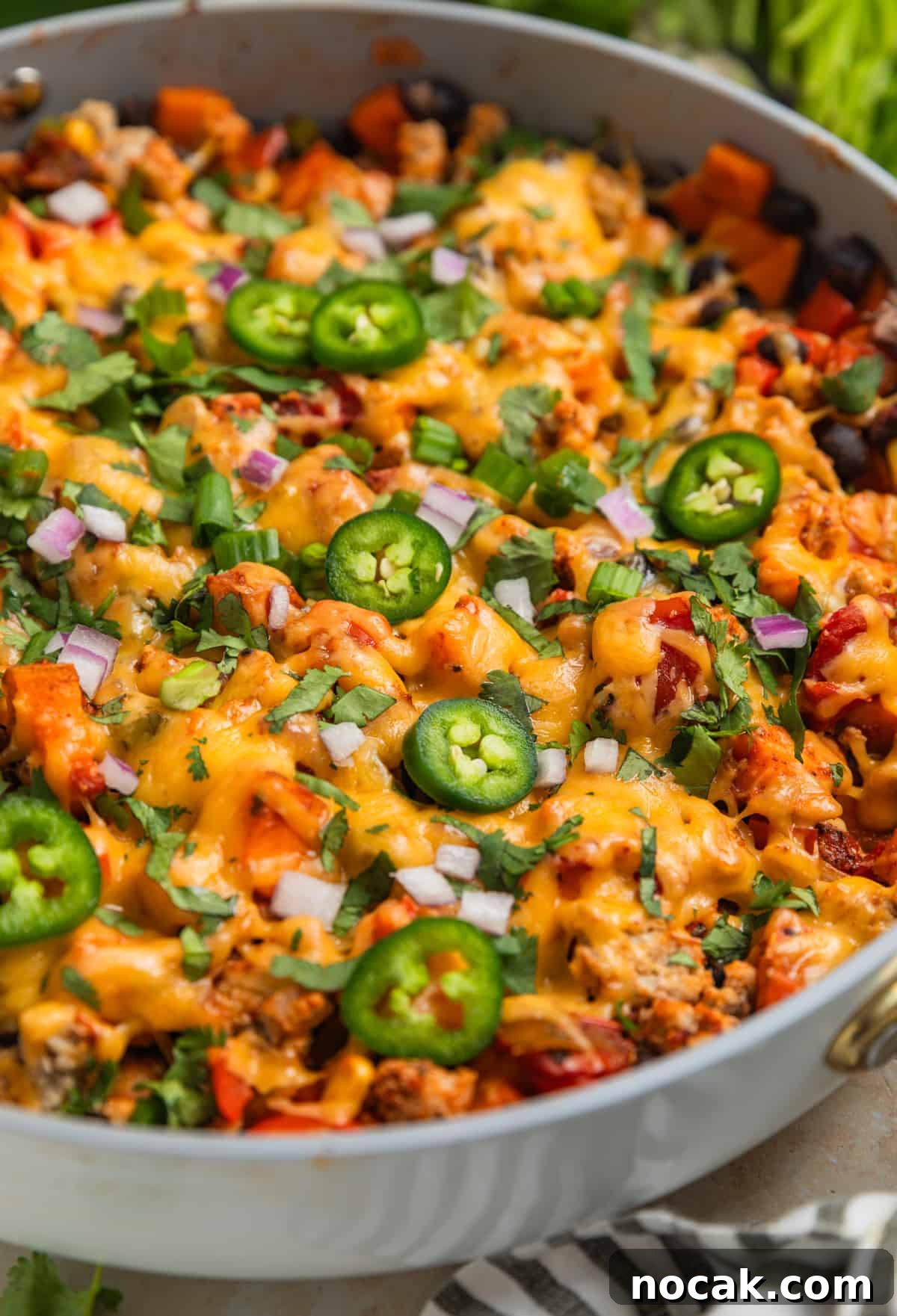 One-Pan Ground Turkey and Sweet Potato Skillet 3 Skillet with cooked meat and vegetables topped with melted cheese, cilantro, peppers, onions and more.