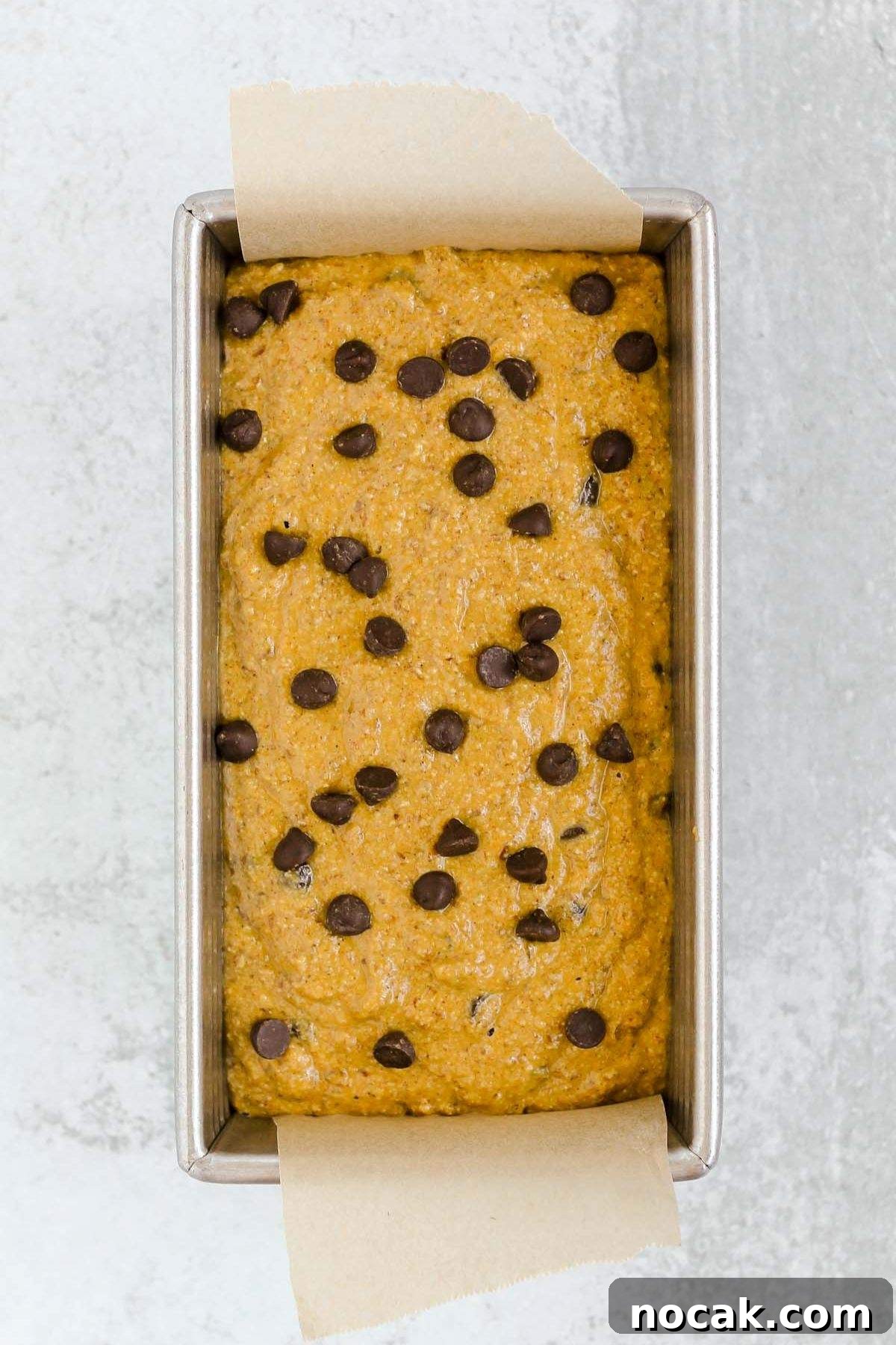 Loaf pan with pumpkin bread batter sprinkled with chocolate chips.