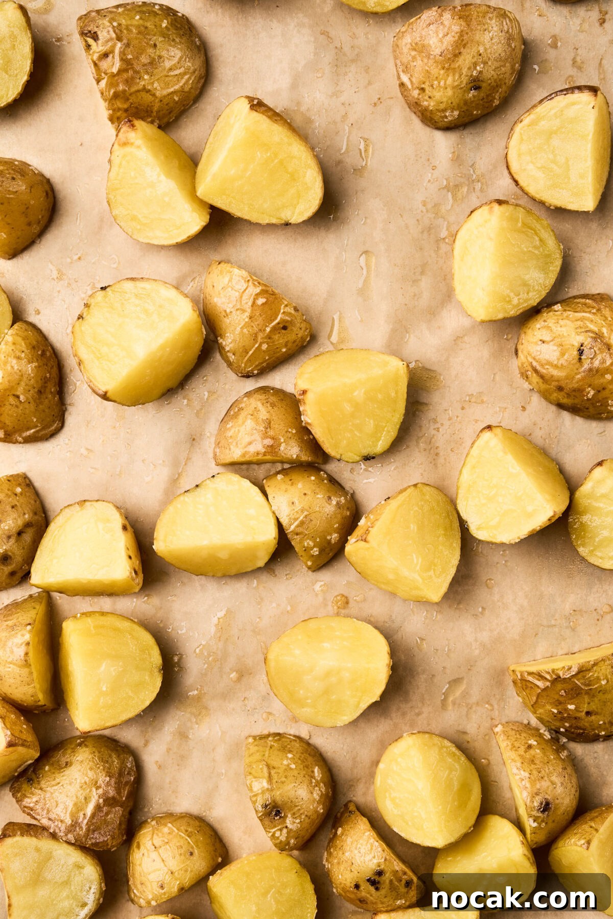 Sheet Pan Chicken Sausage with Roasted Apples 4 Quartered baby gold potatoes arranged on a parchment-lined sheet pan, ready to roast for a chicken sausage with apples recipe.