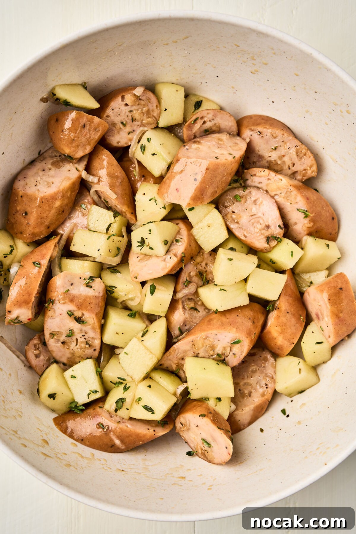 Sheet Pan Chicken Sausage with Roasted Apples 5 Sliced chicken sausage and diced Granny Smith apples tossed with herbs in a mixing bowl for a sheet pan chicken sausage with apples recipe.