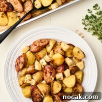 Sheet Pan Chicken Sausage with Roasted Apples 9 Roasted chicken sausage with apples and potatoes served on a white plate with fresh thyme and a sliced apple on the side.