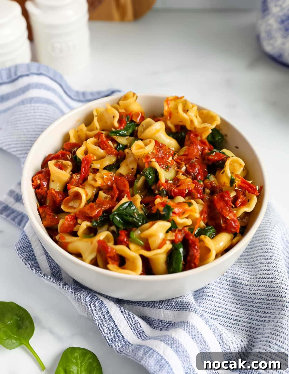 Creamy Tuscan Garlic Pasta with Sun Dried Tomatoes 5 A white bowl filled with cooked pasta topped with a tomato and spinach sauce.