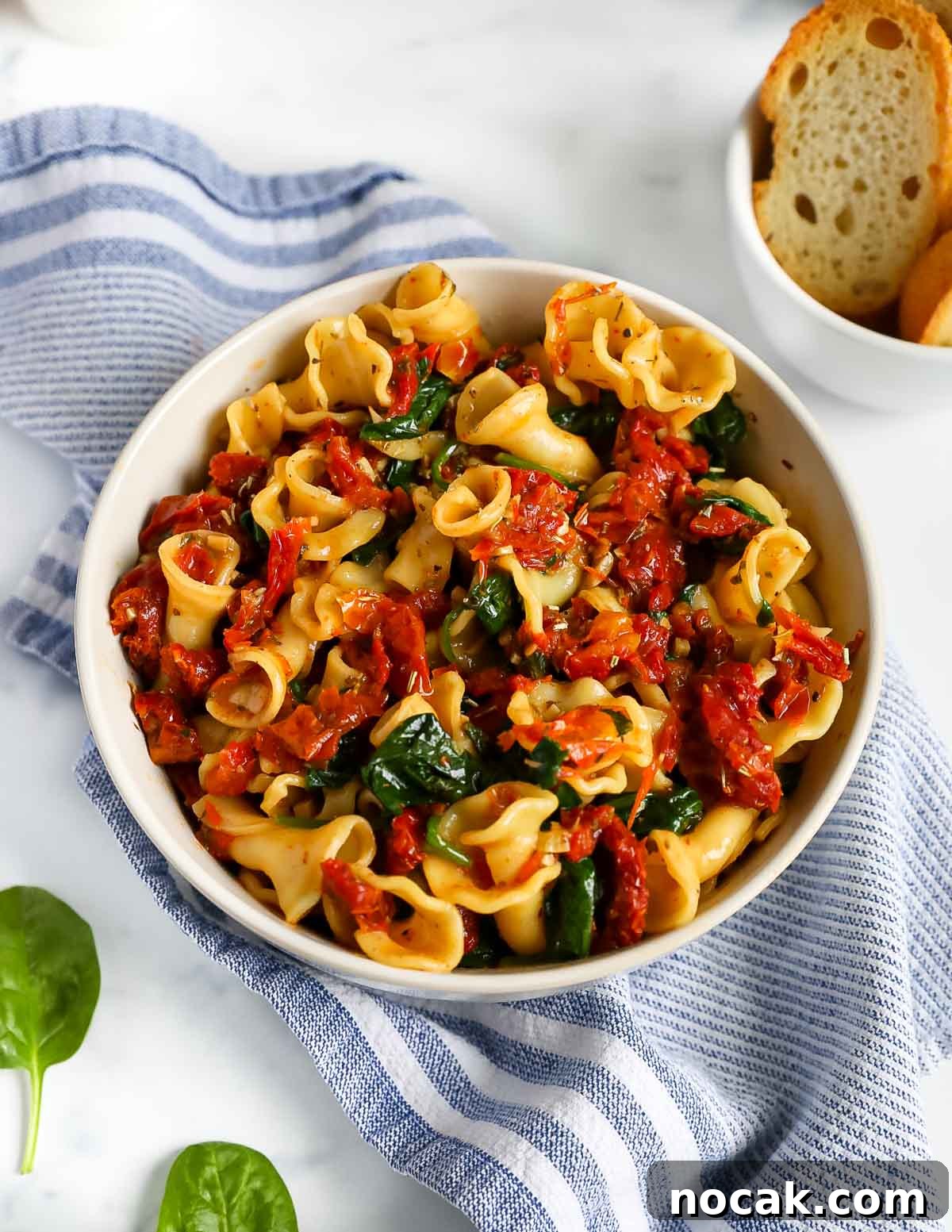 Creamy Tuscan Garlic Pasta with Sun Dried Tomatoes 7 A white bowl with cooked pasta, sun dried tomatoes, and spinach.